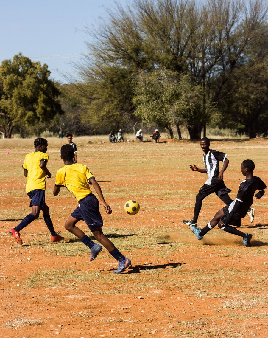 Teenagers playing football on a dirt pitch
